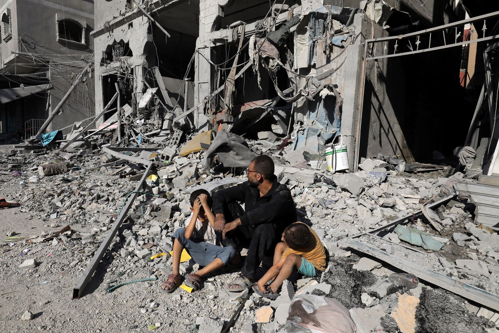 En far og to barn sitter foran et bombet hus i Gaza.