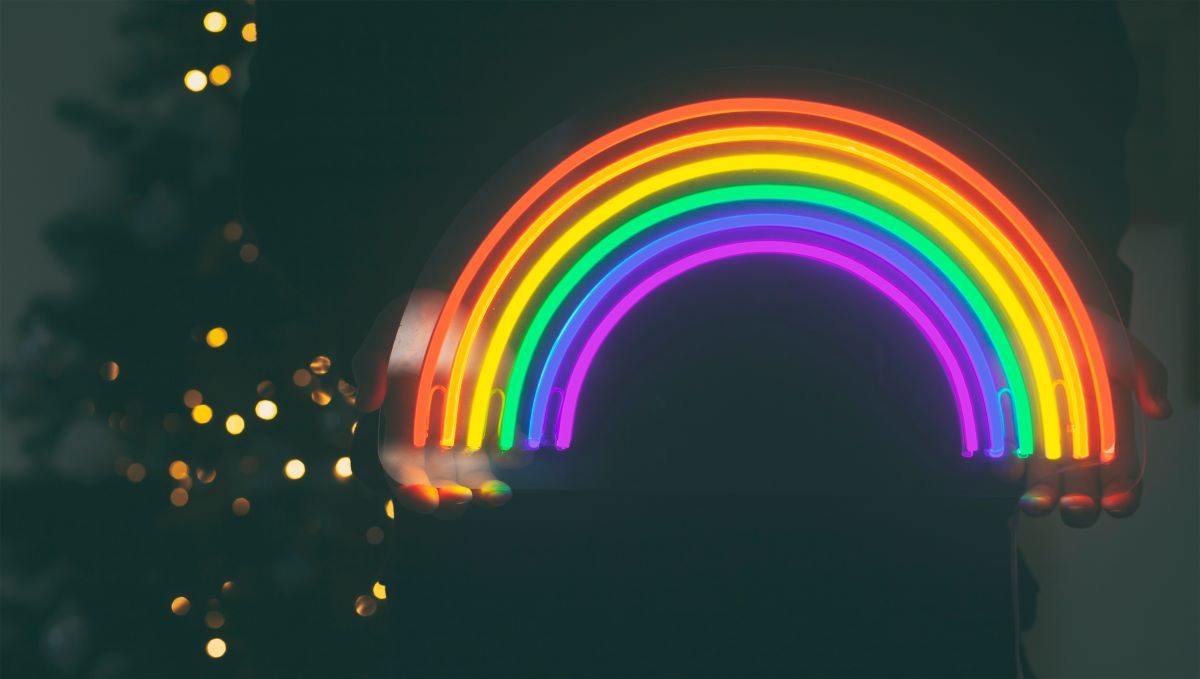 Regnbue i neon i mørket holdt av en kvinne