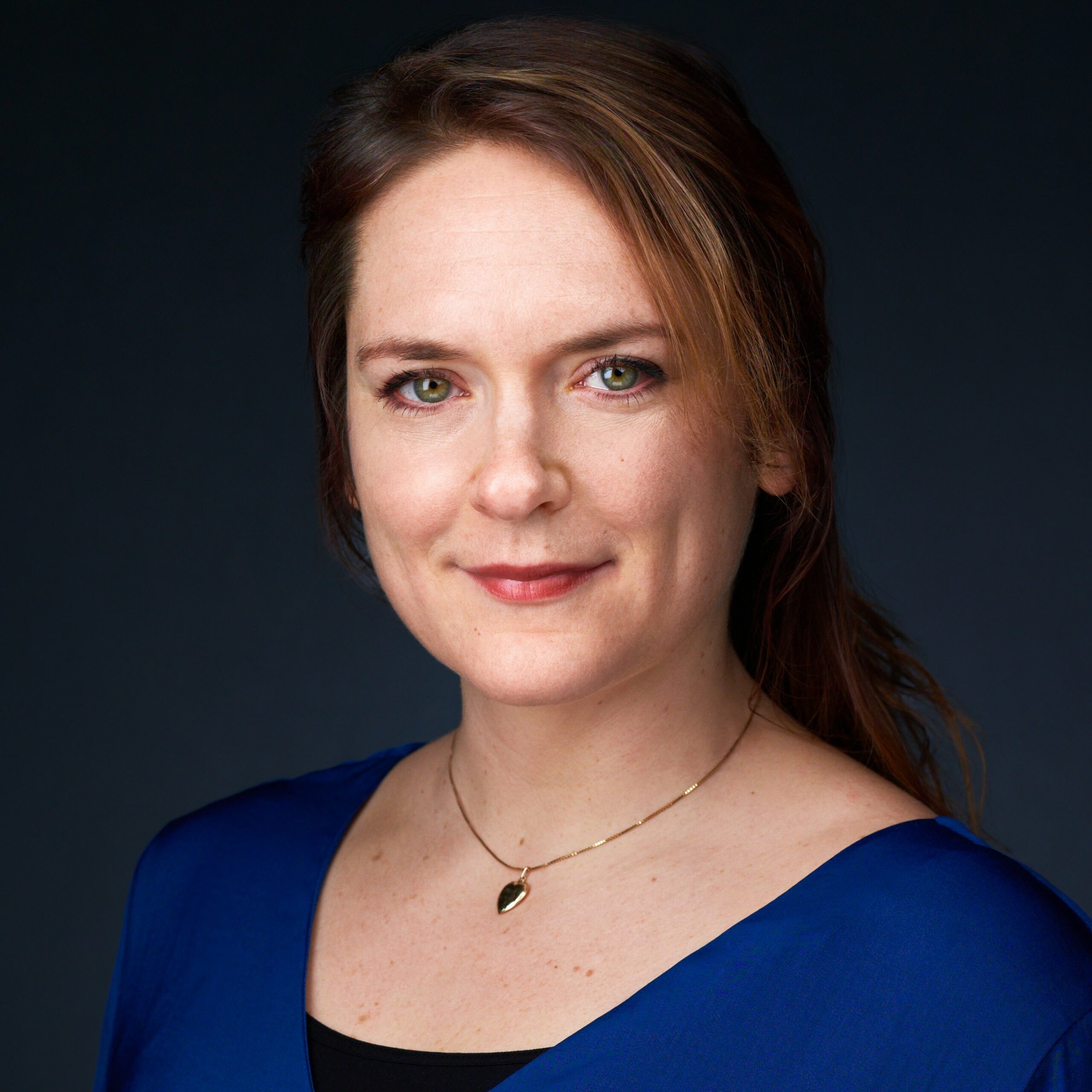 Lise tveter har grønne øyne og rødlig hår, hun har på seg en blå bluse og kjede i halsen