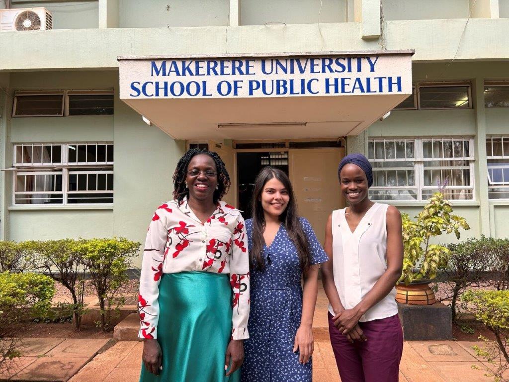 Nora Braathu og to kolleger foran inngangen til Makerere universitet. De smiler.