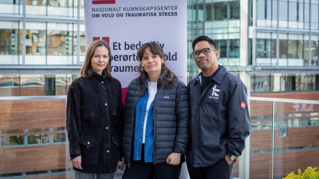 Tre NKVTS-forskere står foran et banner